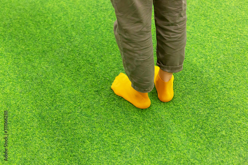 Women's legs with marsh-colored jeans and orange socks stand on a green artificial carpet.