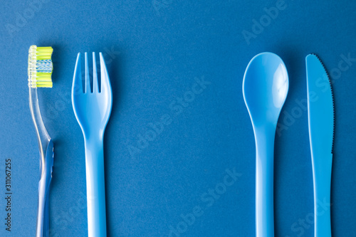 Plastic fork  spoon and knife with toothbrush on blue background meal and oral hygiene abstract.