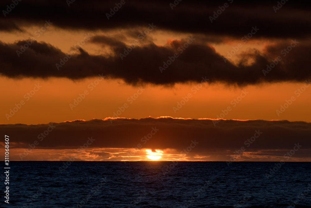 Naklejka premium Natural marine landscape with amazing sunset over the ocean in Tenerife Canary Island Spain. Summer exotic vacation postcard from tropical island. Wonderful orange sunrise over the water behind clouds