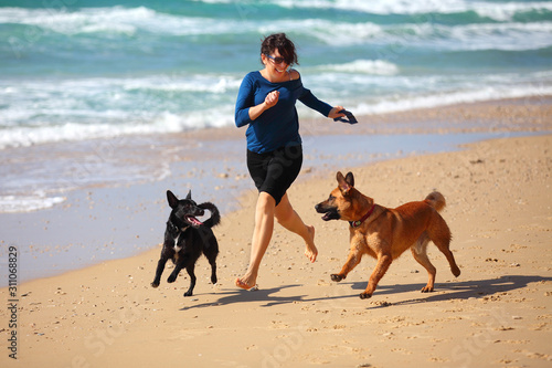Mature Woman  playing with her dogs on the beach.