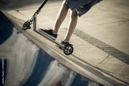 Close up view of tennager's feet riding a scooter making tricks on half pipe. Trendy young skater enjoying outdoors at the skatepark with kick scooter. Youth, freedom, sport joy and carefree concept photo