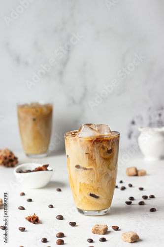 Cold brew coffee with spices and milk on light grey background. Spicy coffee with ice cubes.