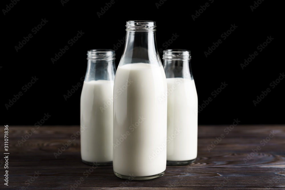 Three glass bottles with milk on a wooden table, black background Three glass bottles with milk on a wooden table, black background