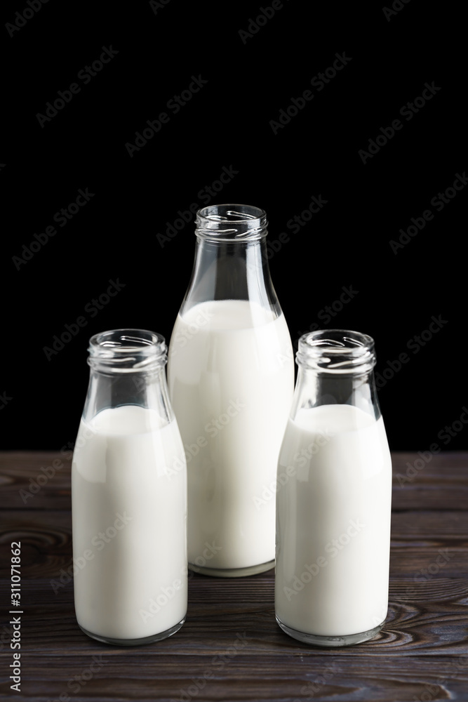 Three glass bottles with milk on a wooden table, black background Three glass bottles with milk on a wooden table, black background