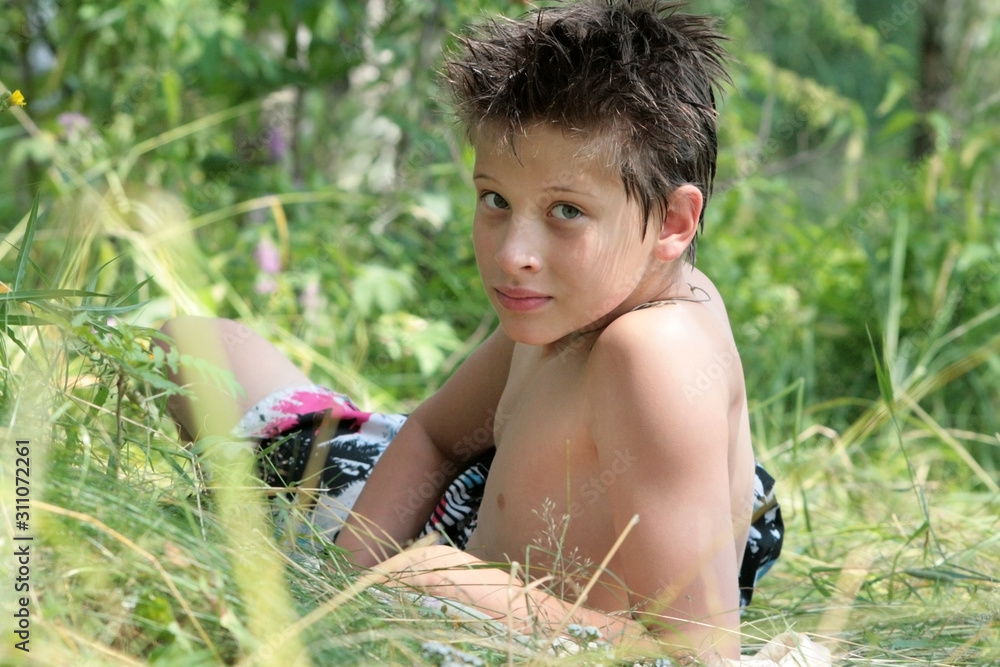A brunette boy lies, sunbathes and looks over his shoulder in the grass