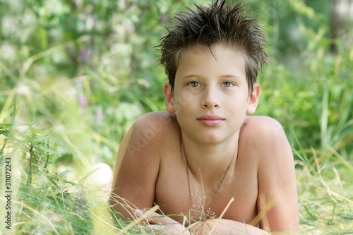 A tanned boy of 12 years old is lying in the grass. Russian	