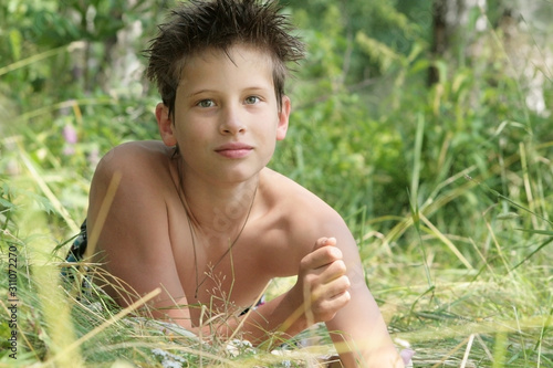 A tanned boy of 12 years old is lying in the grass. Russian	