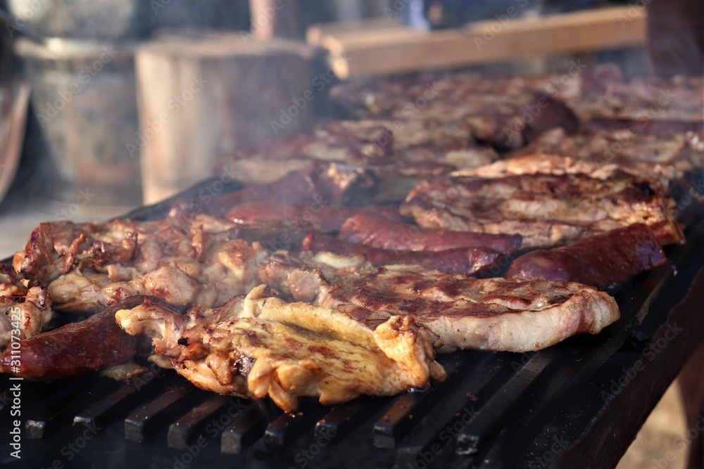 A barbecue where large pieces of meat and sausages are grilled.