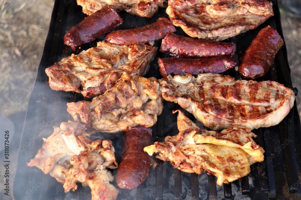 A barbecue where large pieces of meat and sausages are grilled.