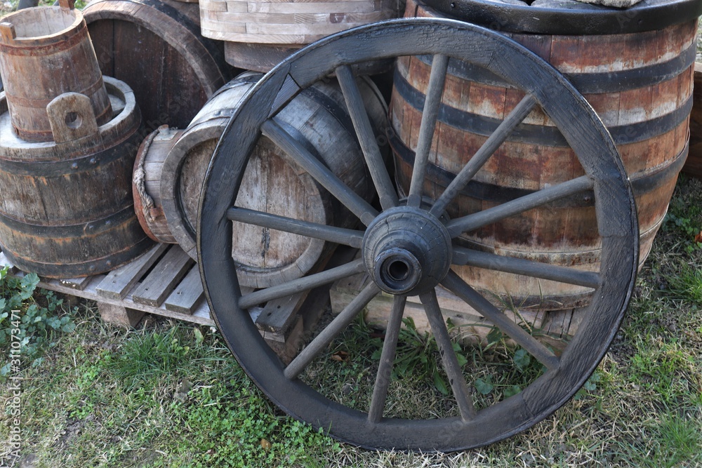 Old wheel from a cart on a background of barrels for wine.