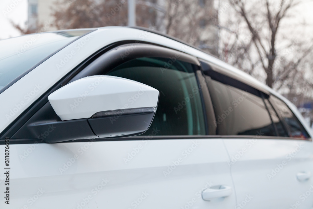 Close-up of the side left mirror and window of the car body white SUV on the street parking after washing and detailing in auto service industry. Road safety while driving