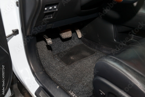 Dirty car floor mats of gray carpet with gas pedals and brakes in the workshop for the detailing vehicle before dry cleaning. Auto service industry. Interior of sedan.