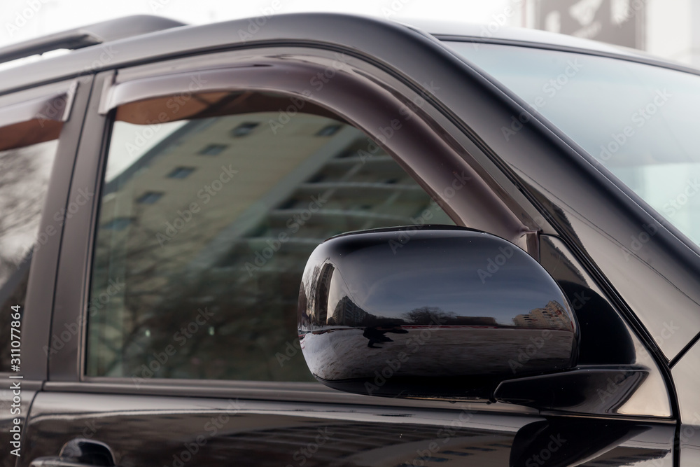 Close-up of the side left mirror and window of the car body black SUV on the street parking after washing and detailing in auto service industry. Road safety while driving