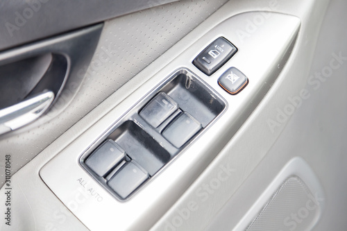 The old bad control buttons for opening and closing windows of doors and electric controls and settings of mirrors on the door in gray with leather upholstery in a luxury modern car.