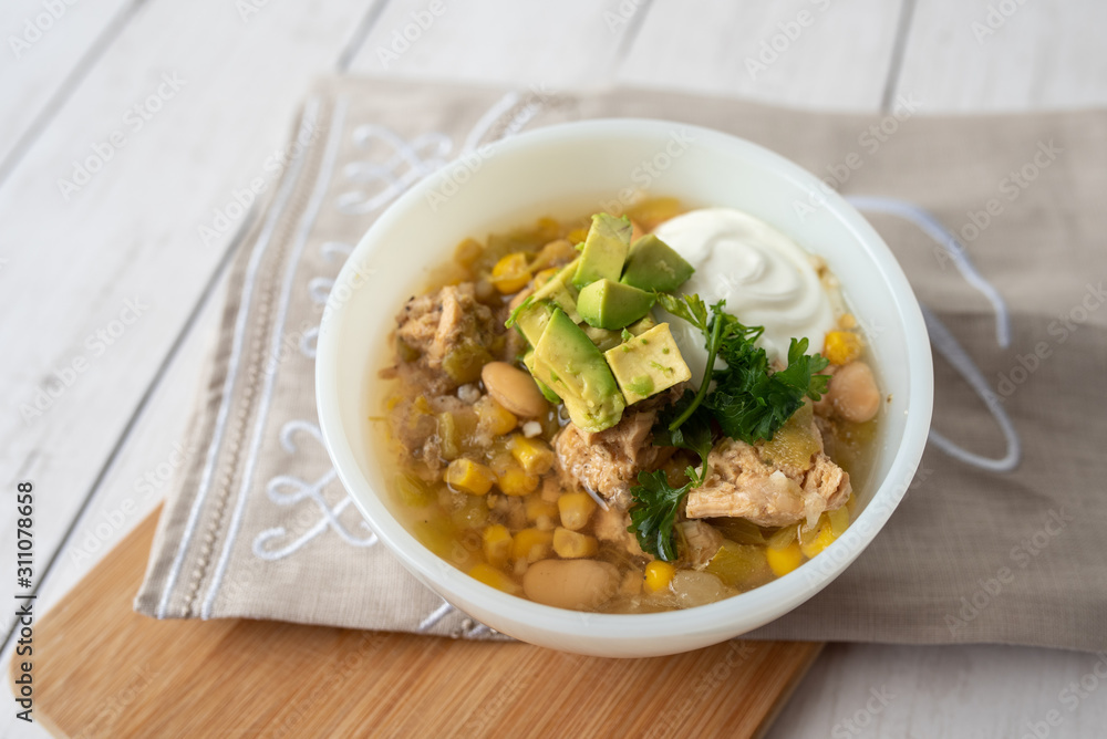 Flavorful White Chicken Chili made with hearty beans, tender chicken, and a rich and creamy broth in slow cooker, garnished with sour cream and avacado Flavorful White Chicken Chili made with hearty beans, tender chicken, and a rich and creamy broth in slow cooker, garnished with sour cream and avacado