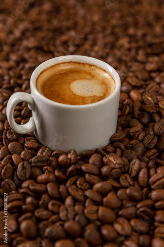 A small white cup of coffee stands on coffee beans. Fragrant pleasure. Background. Space for text. Vertical.