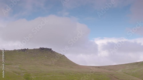 A handheld, wide shot of clouds moving across the sky over the top of a hill in the country side photo