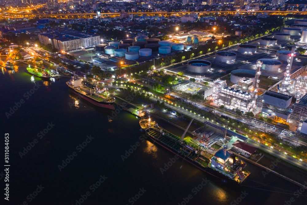 Aerial view oil and gas industrial, Refinery factory oil storage tank and pipeline steel with freight ship at night