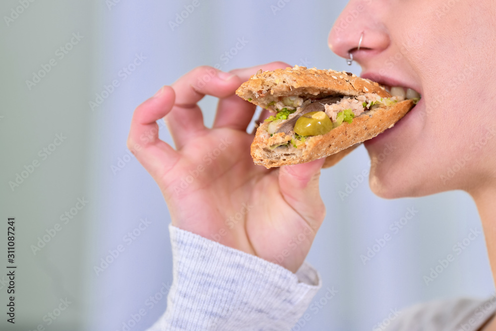 Close-up of a woman biting a tuna sandwich