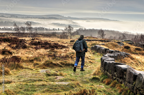 Stone wall and hiker leading into misty Derwent Valley landscape photo