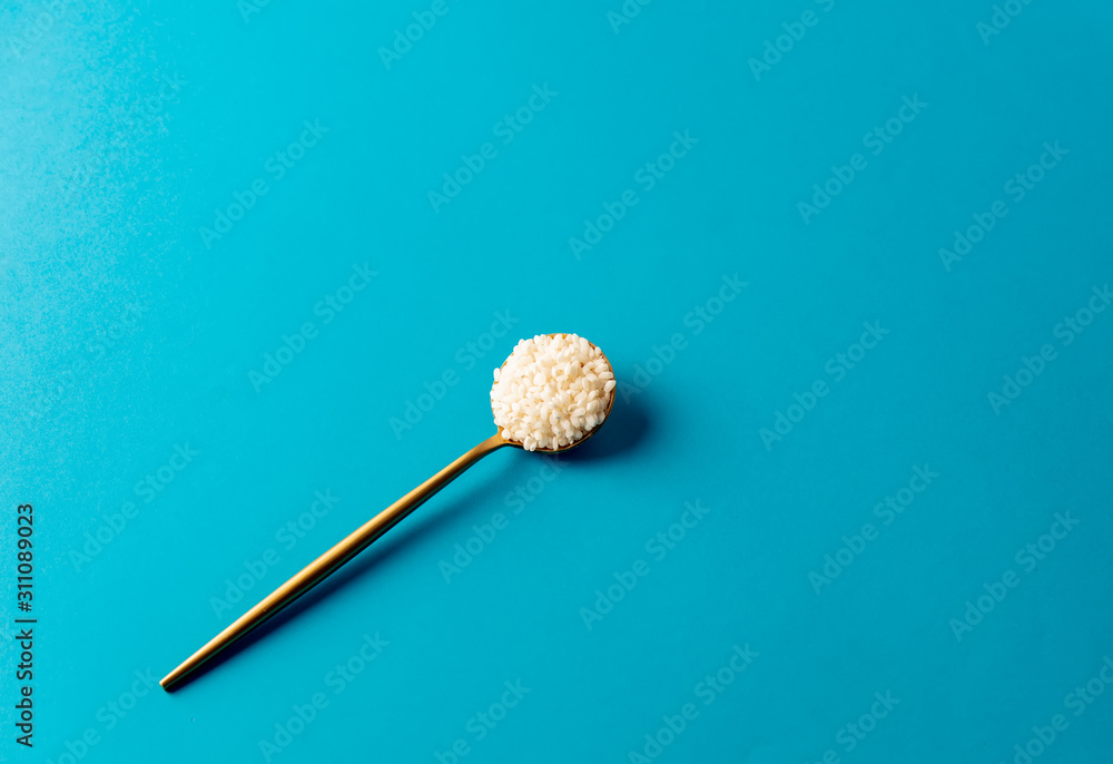 golden spoon with rice grains on blue background golden spoon with rice grains on blue background