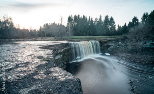 Long exposure photo of Jägala waterfall, 8 meters high and more than 50 meters wide fall in the lower course of the Jägala River. Estonia, Europe. Low sun casts various colors on the water.