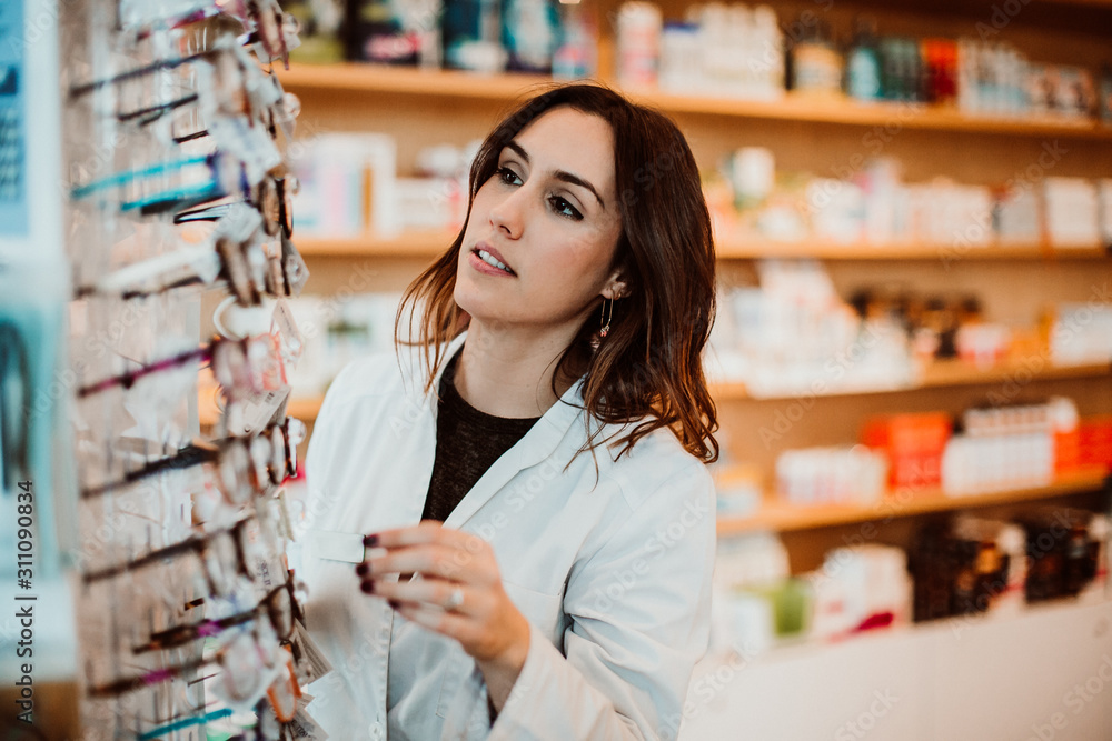 .Young female pharmacist working in her large pharmacy. Placing medications, taking inventory. Lifestyle