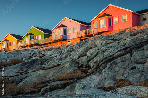 Vibrant wooden houses in Ilulissat, Greenland glowing in warm light on rocky coastal hillside