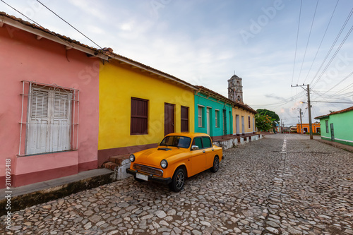 View of an Old Classic Taxi Car in the streets of a small Cuban Town with Church in the Background during a vibrant sunny sunrise. Trinidad, Cuba. © edb3_16