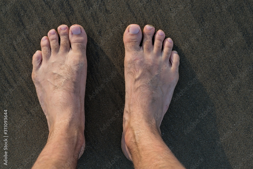 Fototapeta premium Human barefoot feet in wet sand on sea shore, active healthy living and personal growth concept, copy space