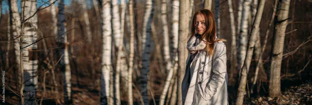 Fototapeta premium Portrait of a girl on the background of trees in early spring at sunset.
