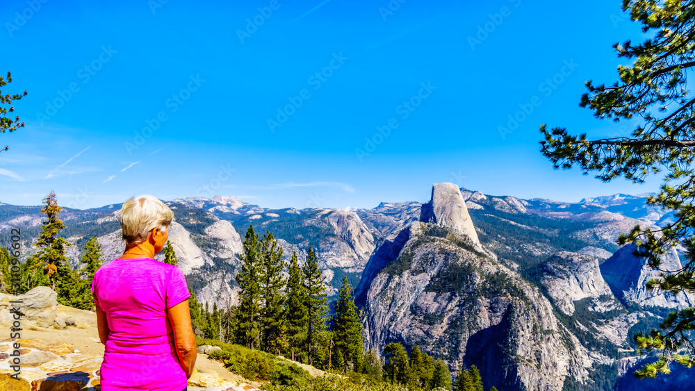 Senior Woman enjoying the view from Glacier Point at the end of Glacier Point Road of the Sierra Nevada high country, with the curved tooth of the famous Half Dome in the foreground in Yosemite Park