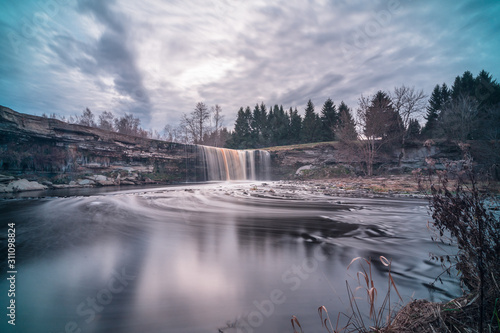 Long exposure photo of Jägala waterfall, 8 meters high and more than 50 meters wide fall in the lower course of the Jägala River. Estonia, Europe. Low sun casts various colors on the water.