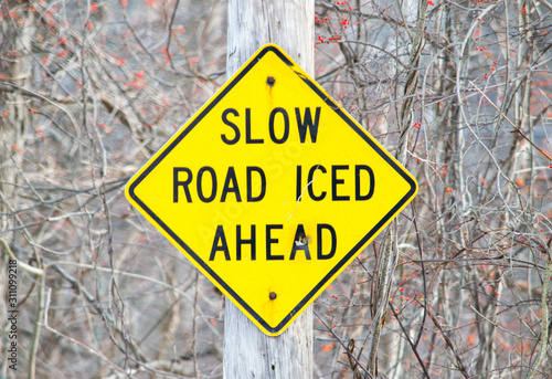 SLOW, ICED AHEAD informational road sign attached to an electric pole, painted in yellow and black colors photo