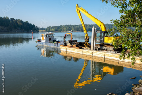 Excavator on floating platform at Ruissalo, Finland is ready for sea dredging work, removing sediment in a waterway. photo