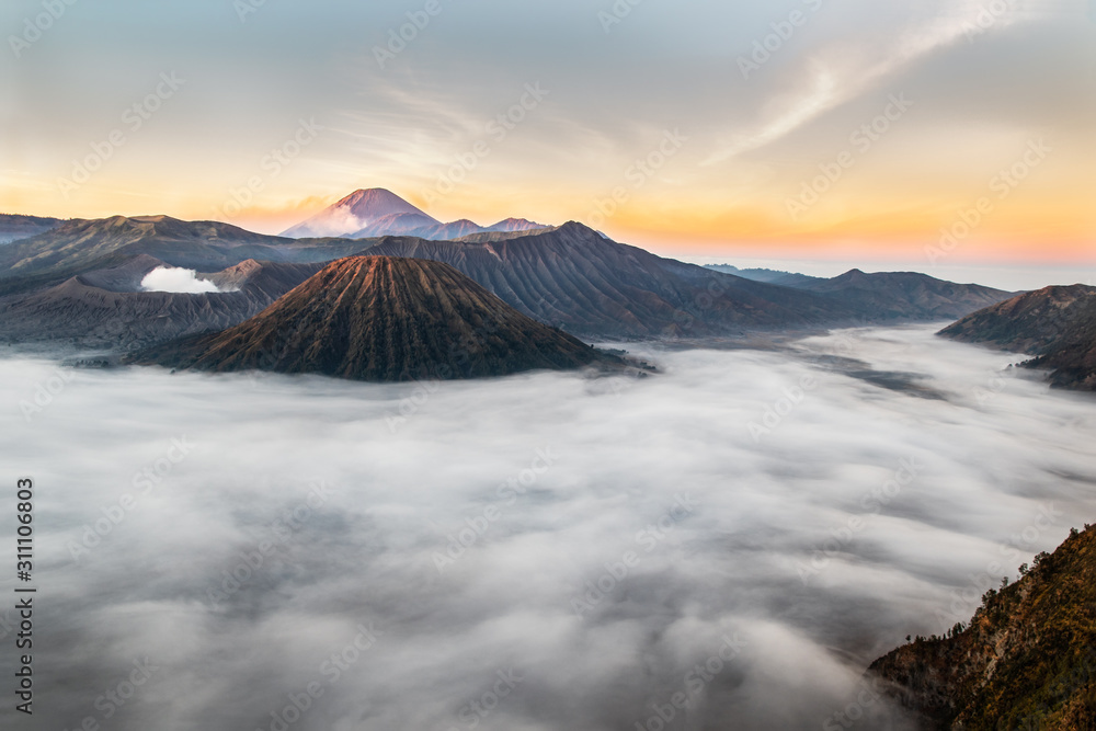 Mount Bromo at sunrise; Island of East Java, Indonesia. Clouds blanket the valley; gas escaping from the crater. Smoke from volcanic peak in the background.