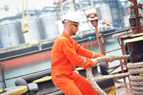 An experienced sailor in orange overalls and a white helmet works on a bulk carrier.