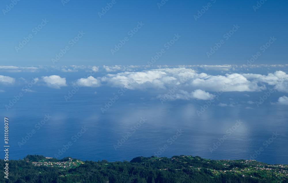 Clouds reflecting from the ocean water during sunrise in Portuguese island Madeira. View from Pico Ruivo path towards Sao Jorge over the dark green slopes of the high mountain array.