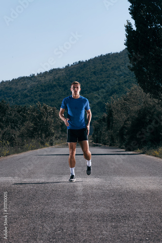 Male athlete running on an empty road in the woods while trying to get to the red finish line.