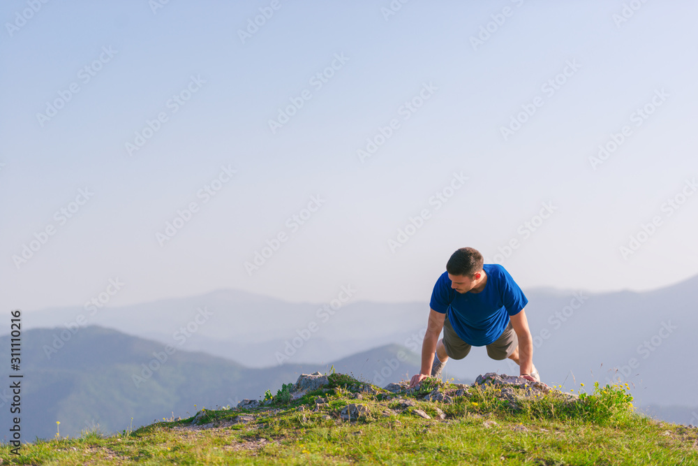 Fit male athlete doing pushups at the edge of a cliff while enjoying the amazing view.