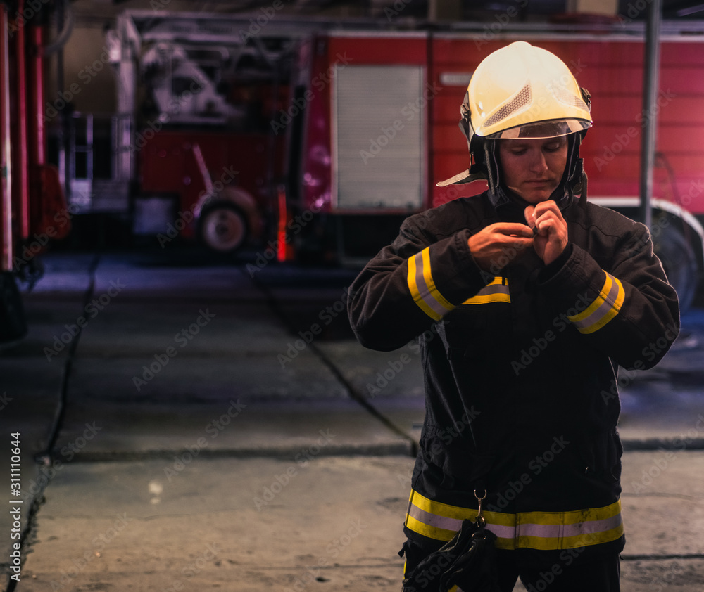 Portrait of young fireman standing inside the fire station. Portrait of young fireman standing inside the fire station.