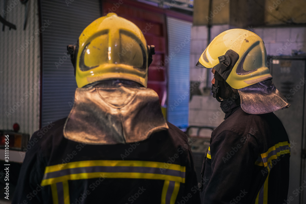 Two young men wearing helmets posing from the back inside the fire station. Two young men wearing helmets posing from the back inside the fire station.