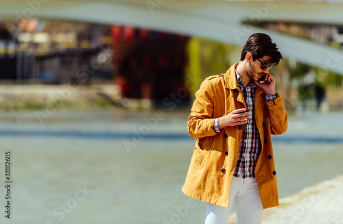 Young manager in yellow coat using his phone near river