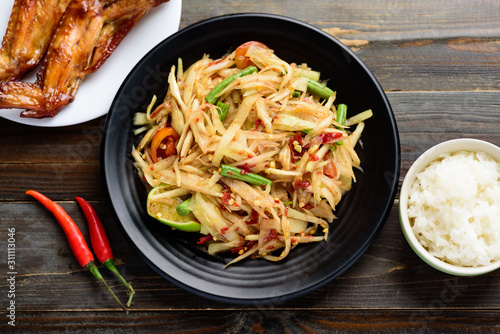 Thai food (Som Tum), spicy green papaya salad eating with grilled chicken wing and sticky rice