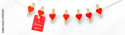 I love you - Clothes pegs with red wooden hearts and paper notes hang on rope isolated on white texture background panorama banner long, with space for text