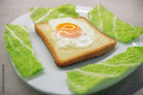 baked egg inside toast bread with lettuce leaves on the sides on a white plate close-up