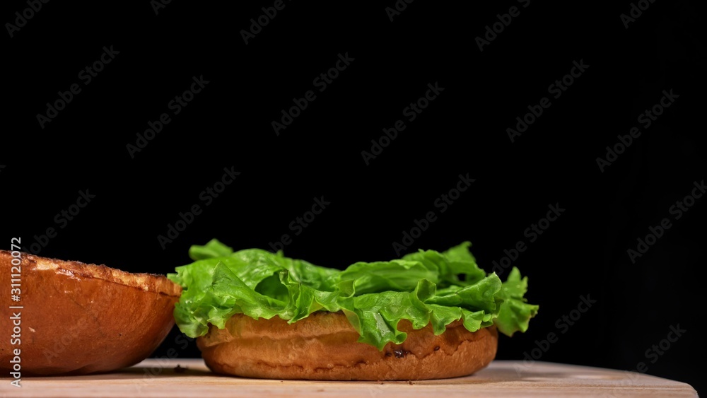 Craft burger is cooking on black background in black food gloves. Consist: sauce, lettuce, tomato, red onion, pickle, cheese, bacon, air bun and marbled meat beef. Not made ideal. Looks real, loving Craft burger is cooking on black background in black food gloves. Consist: sauce, lettuce, tomato, red onion, pickle, cheese, bacon, air bun and marbled meat beef. Not made ideal. Looks real, loving