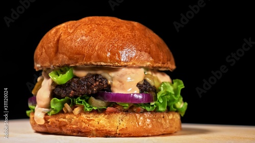 Craft burger is cooking on black background. Consist: red sauce salsa, lettuce, red onion, pickle, cheese, chilli green pepper, air bun and marbled meat beef. Not made ideal. Loving hand made.