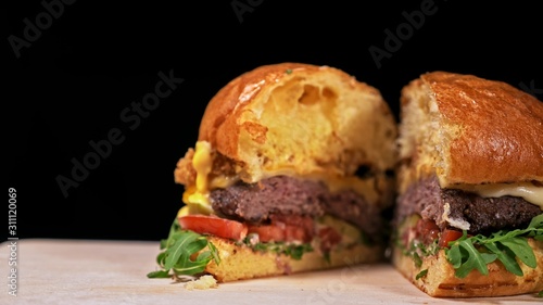 Cut craft burger is cooking on black background in black food gloves. Consist: sauce, arugula, tomato, red onion rings fries, cucumber, cheese, air bun and marble meat beef. Not made ideal. Looks real