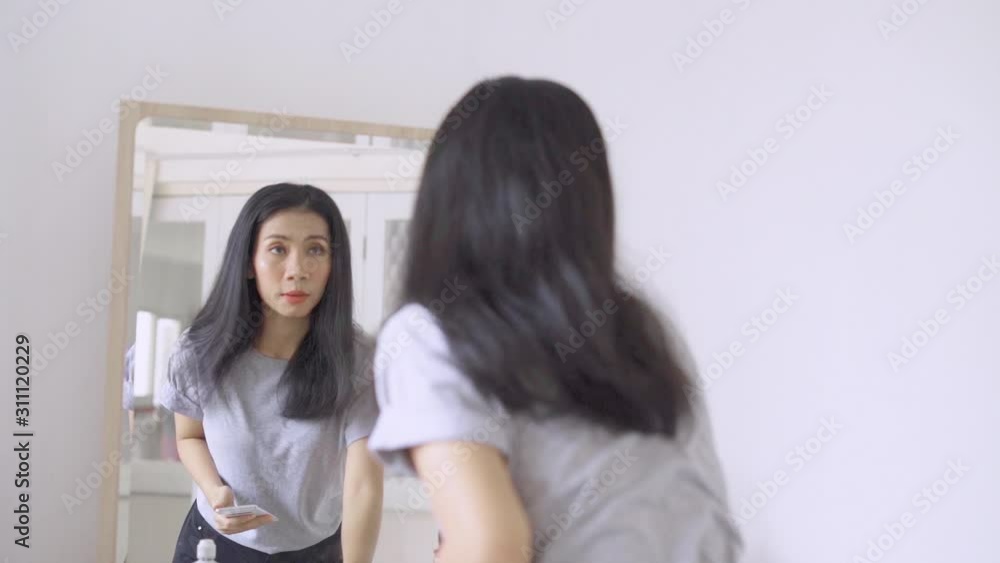 Slow motion of young woman combing her hair in front of the mirror while using a mobile phone in makeup room Slow motion of young woman combing her hair in front of the mirror while using a mobile phone in makeup room